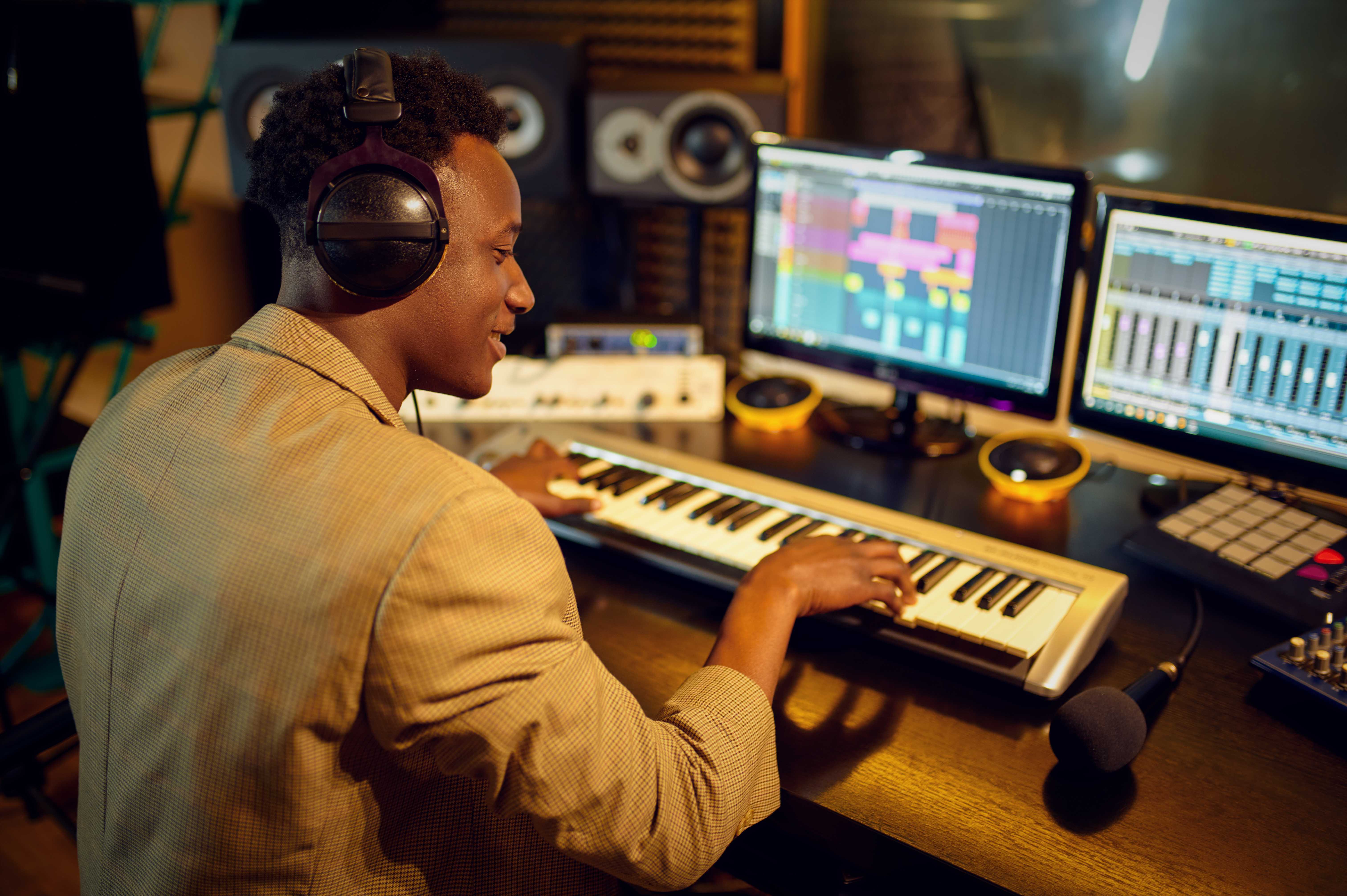 man sitting behind a studio desk wearing headphones and playing on a small midi keyboard.